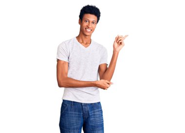 Beyaz tişört giyen genç Afro-Amerikalı adam gülümsüyor mutlu bir şekilde elini ve parmağını yana doğru gösteriyor. 