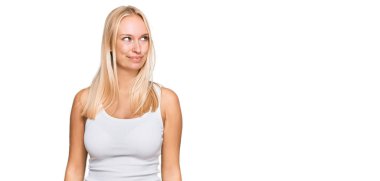 Sıradan giyinen, kolsuz tişörtlü, gülümseyen, yan bakan ve düşünen genç sarışın kız.. 