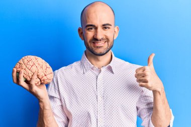 Beyni gülen, mutlu ve olumlu gülümseyen genç ve kel bir adam. Başparmağıyla mükemmel ve onay işareti yapıyor. 