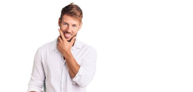 Gündelik kıyafetler giyen genç beyaz adam kameraya kendinden emin bakıyor kollarını kavuşturmuş ve çenesini kaldırmış gülümsüyor. Olumlu düşünmek. 