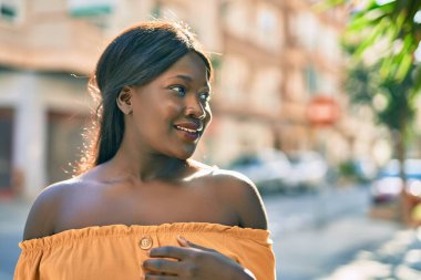 Genç Afrikalı Amerikalı kadın gülümseyerek şehirde mutlu mesut duruyor..