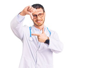 Doktor üniforması giyen yakışıklı genç adam gülümseyerek elleri ve parmakları gülen yüzüyle çerçeve yapıyor. yaratıcılık ve fotoğrafçılık kavramı. 