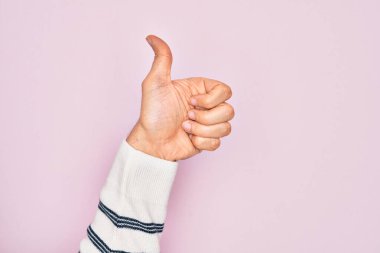 İzole edilmiş pembe arka planda parmaklarını gösteren beyaz bir gencin eli başarılı bir onay jesti yapıyor. Başparmak işareti, onaylama ve olumlu bir sembol.