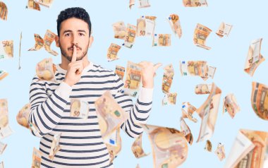 Gündelik giysiler giyen genç İspanyol adam sessiz olmak istiyor. Parmakları dudaklarında, elleri yandan işaret ediyor. sessizlik ve gizli konsept.