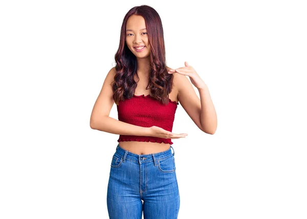 若い美しい中国の女の子を身に着けているカジュアル服ジェスチャーで手を示す大小のサイン メジャーシンボル カメラを見て笑ってる 概念を測定し — ストック写真