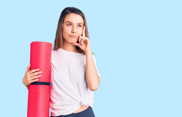 Joven Hermosa Chica Sosteniendo Alfombra Yoga Cara Seria Pensando Pregunta — Foto de Stock