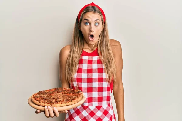 Jovem Loira Vestindo Avental Profissional Padeiro Segurando Pizza Italiana Assustada — Fotografia de Stock