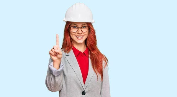 Joven Pelirroja Vestida Con Arquitecto Hardhat Mostrando Señalando Hacia Arriba — Foto de Stock