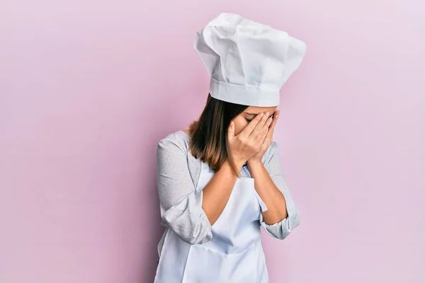 年轻美丽的女人穿着职业厨师的制服和帽子 脸上挂着悲伤的表情 一边哭一边用手捂住脸 抑郁症的概念 — 图库照片