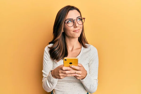 Młoda Brunetka Kobieta Pomocą Smartfona Żółtym Tle Uśmiecha Się Patrząc — Zdjęcie stockowe