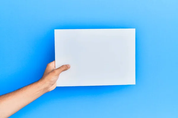 Mão Jovem Hispânico Segurando Banner Vazio Sobre Fundo Azul Isolado — Fotografia de Stock