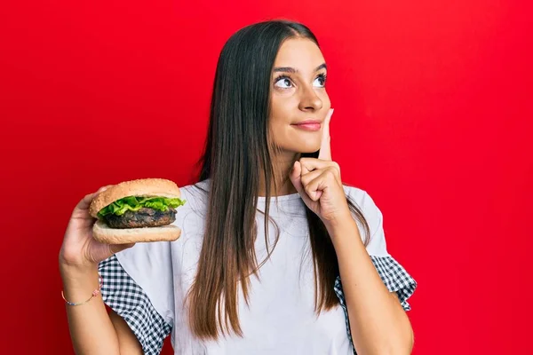 Mujer Hispana Joven Comiendo Hamburguesa Cara Seria Pensando Pregunta Con —  Fotos de Stock