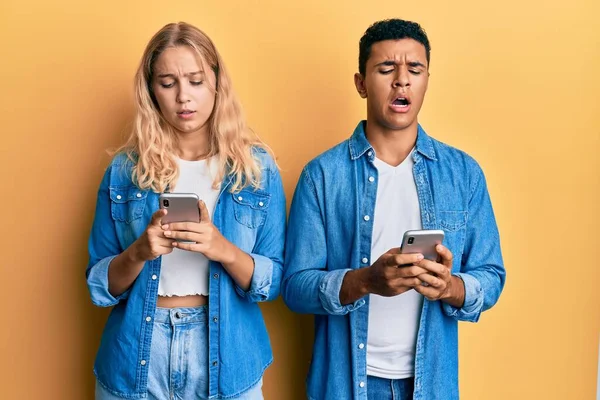 Şok suratlı akıllı telefon kullanan, kuşkucu ve alaycı bakışlı, ağzı açık genç bir çift. 