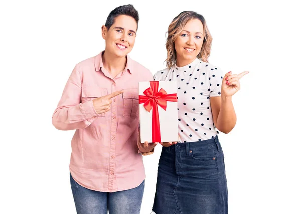 Pareja Mujeres Sosteniendo Regalo Sonriendo Feliz Señalando Con Mano Dedo —  Fotos de Stock