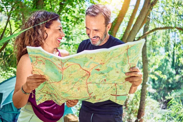 Middle age couple  of hiker camping at the forest. Standing with smile on face looking at the map.