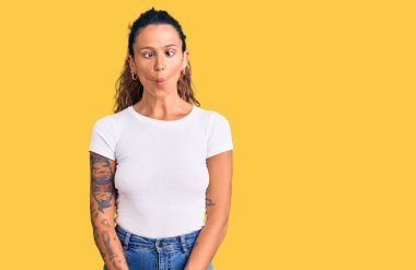 Gündelik beyaz tişörtlü, dudakları balık suratlı, çılgın ve komik bir jest yapan İspanyol bir kadın. Komik ifade. 