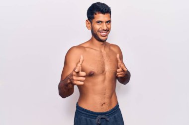 Genç latin adam, tişörtsüz bir şekilde kamerayı mutlu ve komik yüzüyle işaret ediyor. iyi enerji ve titreşimler. 