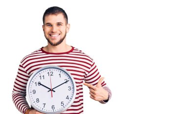 Büyük saati tutan yakışıklı genç adam gülümsüyor. 