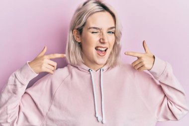 Genç sarışın kız, parmaklarını şıklatarak kameraya bakıyor. Seksi bir ifadeyle, neşeli ve mutlu bir yüzle.. 