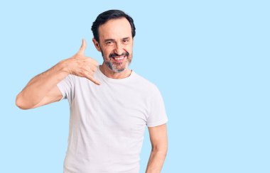 Orta yaşlı yakışıklı bir adam günlük tişört giyiyor gülümsüyor telefonla el ve parmak hareketleri yapıyor telefonda konuşuyor gibi. iletişim kavramları. 