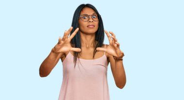 Genç Afro-Amerikalı kadın günlük kıyafetler ve gözlük takıyor. Korkudan dehşete düşmüş ve korkmuş. El hareketlerini durdur, şok içinde bağır. panik konsepti. 