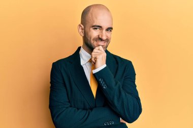 Genç İspanyol takım elbiseli ve kravatlı adam kameraya kendinden emin bakıyor kollarını kavuşturmuş ve çenesini kaldırmış bir şekilde gülümsüyor. Olumlu düşünmek. 