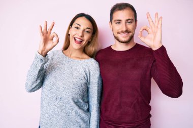 Gündelik giysiler giyen güzel bir çift pozitif gülümsüyor ve el ve parmaklarıyla 