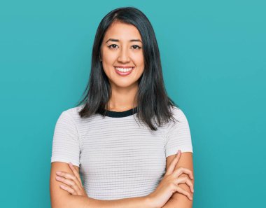 Sıradan beyaz tişört giyen güzel Asyalı genç kadın kollarını kavuşturup kameraya bakarken gülümsüyor. pozitif kişi. 