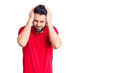 Sakallı, gündelik tişörtlü, baş ağrısı çeken, çaresiz ve stresli genç bir adam. Ağrı ve migren yüzünden. Eller başının üstünde.. 