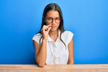 Gündelik kıyafetler giyen güzel İspanyol kadın masanın ağzında oturuyor ve dudakları parmaklarıyla fermuar gibi kapalı. gizli ve sessiz, tabu konuşması 