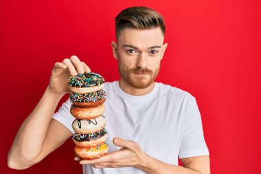 Genç kızıl saçlı adam elinde lezzetli renkli çörekler tutuyordu. Yüzünde ciddi bir ifadeyle gevşemişti. Basit ve doğal bir şekilde kameraya bakıyorsun.. 