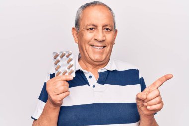 Yaşlı adam elinde haplar tutarken mutlu bir şekilde gülümsüyor. 