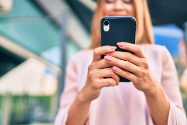 Genç beyaz kız şehirde akıllı telefon kullanarak mutlu bir şekilde gülümsüyor..