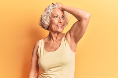 Kıdemli gri saçlı kadın, günlük kıyafetler giyiyor, gülümsüyor, saçlarına dokunuyor, el hareketi yapıyor, çekici ve modaya uygun poz veriyor. 