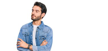 Sıradan kıyafetler giyen genç İspanyol adam kollarını kavuşturmuş ve kendinden emin bir şekilde yan tarafa bakıyor. 