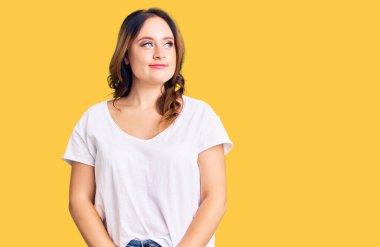 Beyaz bir tişört giyen genç, güzel, beyaz bir kadın gülümsüyor, yan tarafa bakıyor ve düşünüyor.. 
