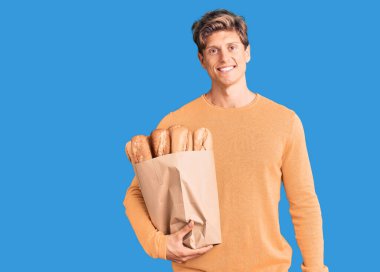 Elinde ekmek dolu kese kağıdıyla genç ve yakışıklı bir adam. Pozitif ve mutlu görünüyor. Kendine güvenen bir gülümsemeyle, dişlerini gösteriyor. 