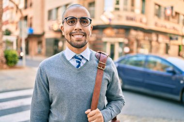 Genç Afrikalı Amerikalı iş adamı gülümseyerek şehirde mutlu bir şekilde yürüyor..