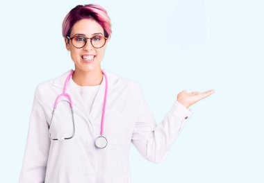 Pembe saçlı, doktor üniforması giyen, neşeli gülümseyen, avuç içi kameraya bakan genç ve güzel bir kadın.. 