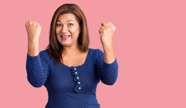 Orta yaşlı Latin kadın gündelik giysiler içinde gururla bağırıyor, zaferi kutluyor ve kollarını kaldırarak çok heyecanlanıyor. 