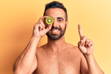 İspanyol asıllı genç üstsüz bir adam elinde kivi, elinde bir fikirle gülümsüyor ya da bir soru işareti yapıyor. 