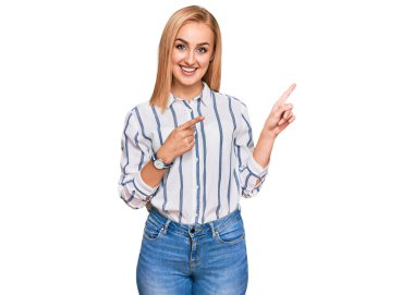 Güzel, beyaz bir kadın, günlük kıyafetler giymiş, gülümseyen ve kameraya bakıp iki elini ve parmağını yana doğru gösteren.. 