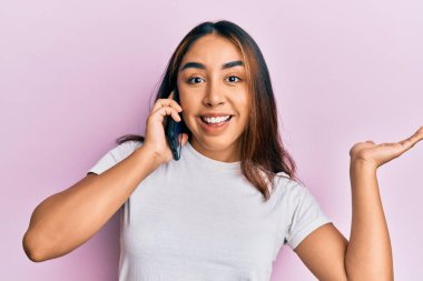 Genç Latin bir kadın akıllı telefonda konuşuyor başarıyı mutlu bir gülümsemeyle kutluyor ve kazanan el kaldırarak ifade ediyor. 