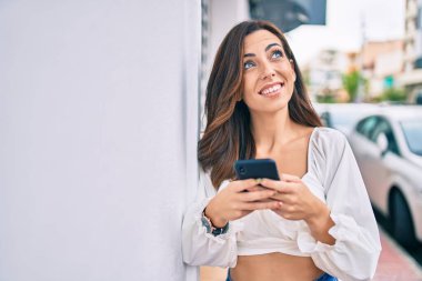 Genç İspanyol kadın şehirde akıllı telefon kullanarak mutlu bir şekilde gülümsüyor..