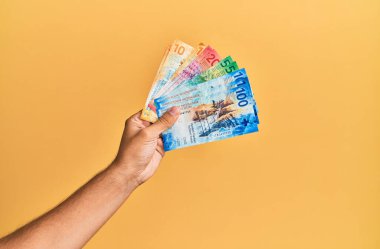 İzole edilmiş sarı arka planda İsviçre frangı banknotları tutan İspanyol bir adam..