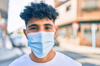 Tıbbi maske takan genç bir Arap, şehrin caddesindeki kameraya bakıyor..