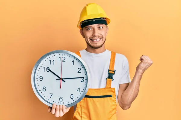 Joven Hispano Vistiendo Uniforme Constructor Sombrero Fuerza Sosteniendo Reloj Gritando —  Fotos de Stock