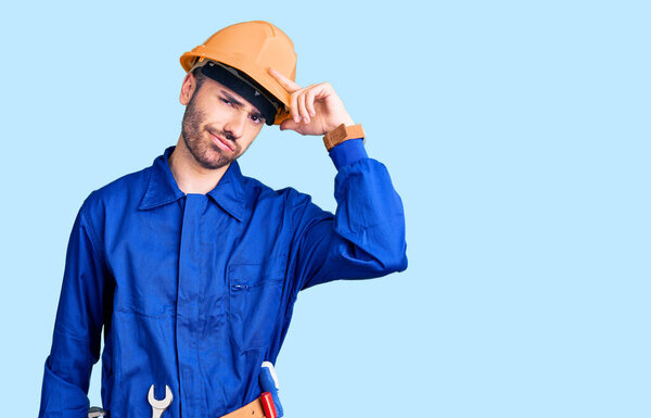 Молодой латиноамериканец, одетый в рабочую форму, беспокоился и переживал о проблеме с рукой на лбу, нервничал и беспокоился о кризисе. 