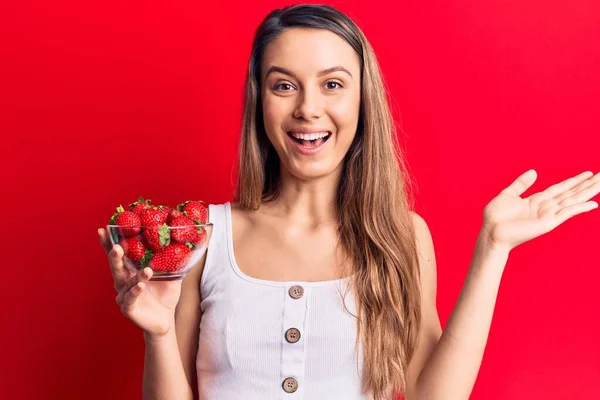 年轻美丽的姑娘拿着盛满草莓的碗 笑容满面 高举双手庆祝胜利 — 图库照片