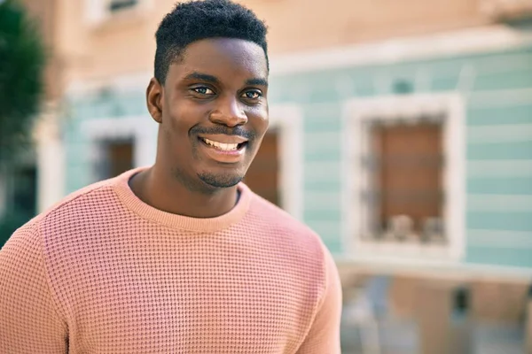 Genç Afrikalı Amerikalı adam gülümseyerek şehirde mutlu mesut duruyor..